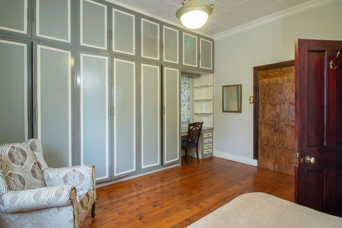 A bedroom featuring extensive built-in cabinetry with an integrated vanity, original hardwood flooring, and a decorative pressed ceiling.