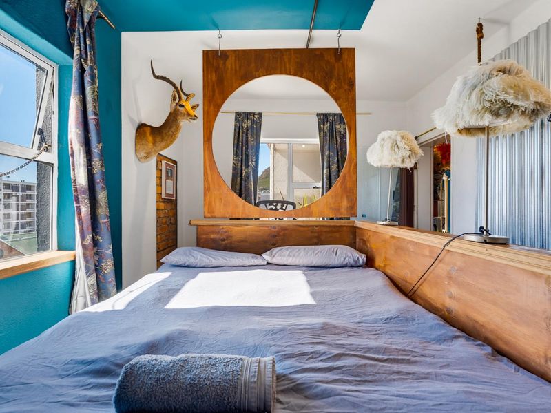 A bedroom featuring a unique wooden room divider, exposed brick accents, and corrugated metal wall paneling with natural light from a side window.