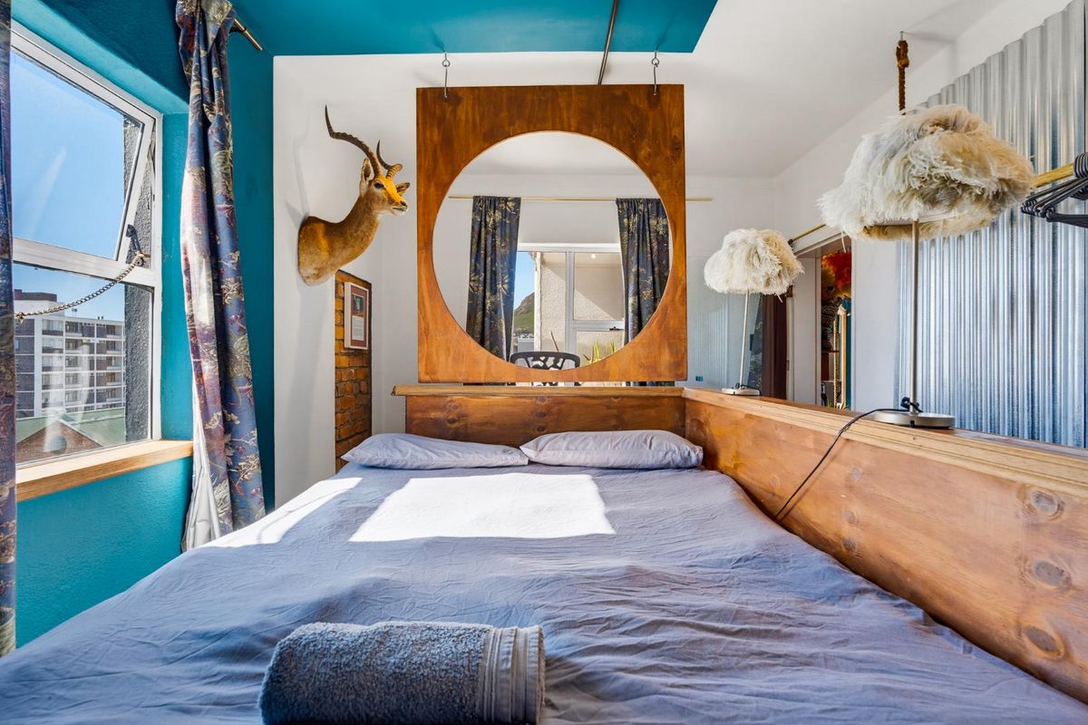 A bedroom featuring a unique wooden room divider, exposed brick accents, and corrugated metal wall paneling with natural light from a side window.