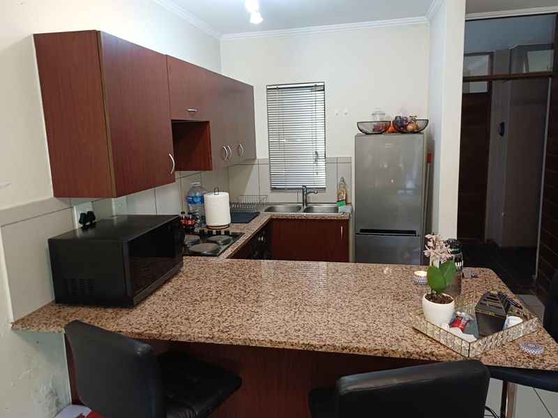 Compact kitchen featuring dark wood cabinetry, granite countertops, a breakfast bar, and a stainless steel double sink with a window view.