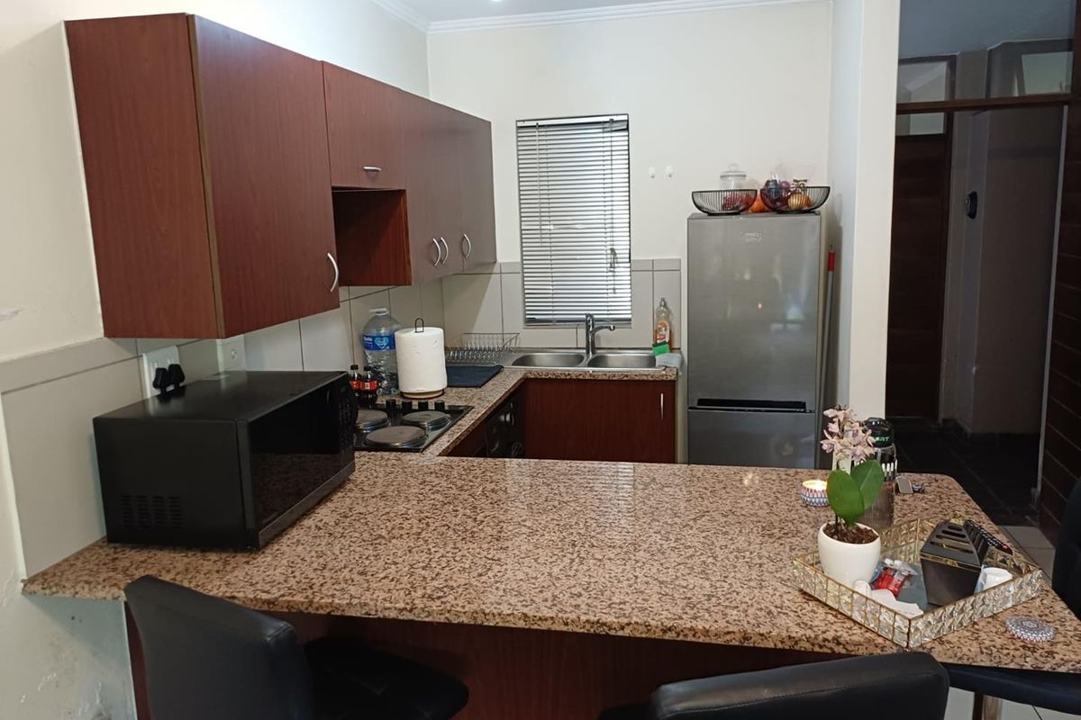 Compact kitchen featuring dark wood cabinetry, granite countertops, a breakfast bar, and a stainless steel double sink with a window view.