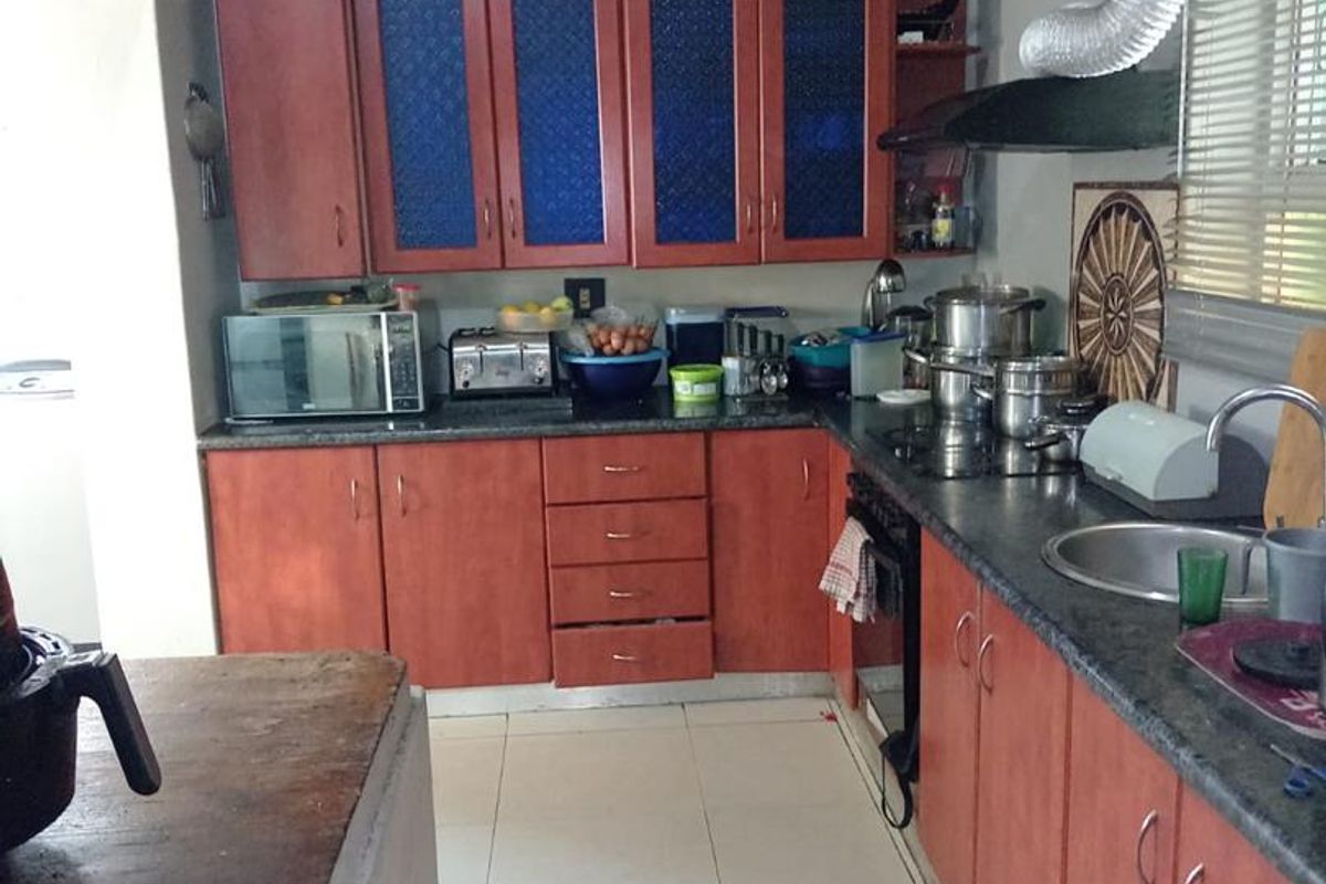 A functional kitchen featuring wood-tone cabinetry, dark countertops, tiled flooring, and an exposed ventilation system.