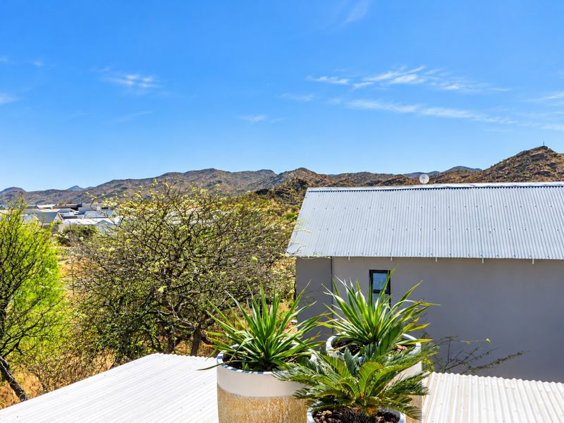Elevated view overlooking the surrounding landscape and mountains, featuring a corrugated metal roof and clear blue sky.