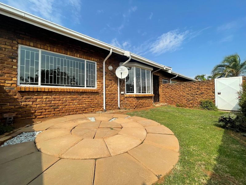 Rear exterior view of a face brick townhouse featuring a circular paved patio area, established lawn, and secure boundary walling.