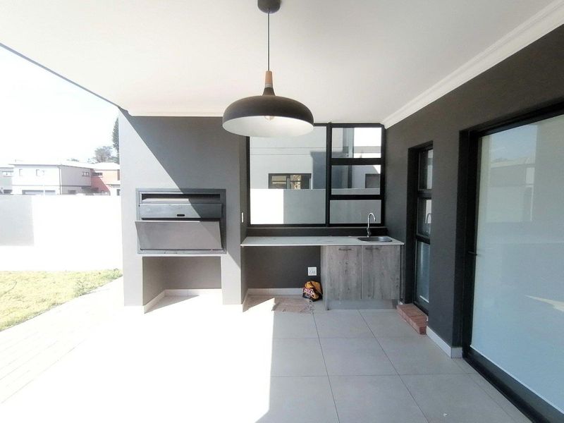 A modern covered patio featuring a built-in braai, a functional prep area with a sink and cabinetry, and large sliding doors leading indoors.