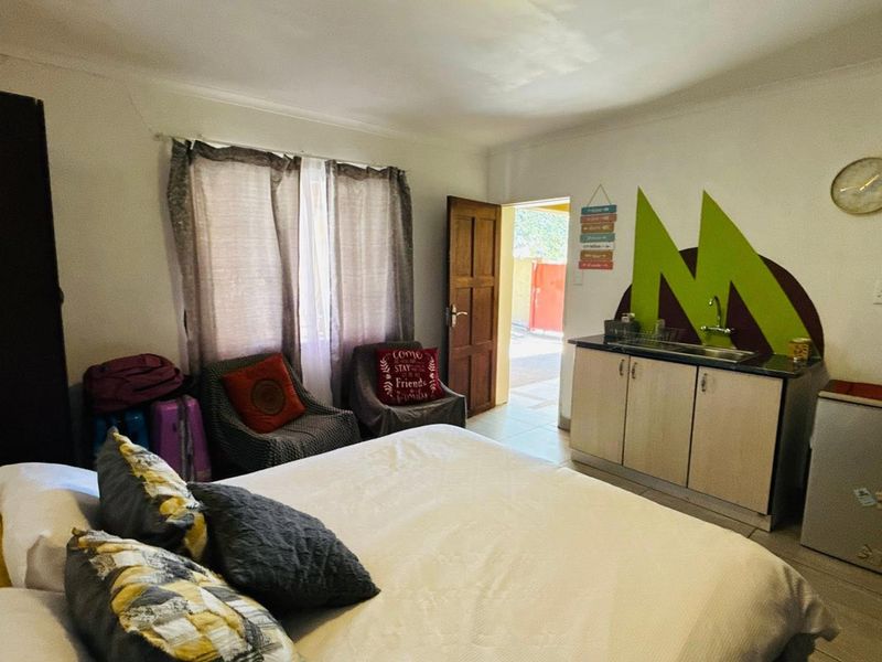 A bedroom featuring a small built-in kitchenette area with a sink and cabinet, tiled flooring, and direct access to an outdoor space.