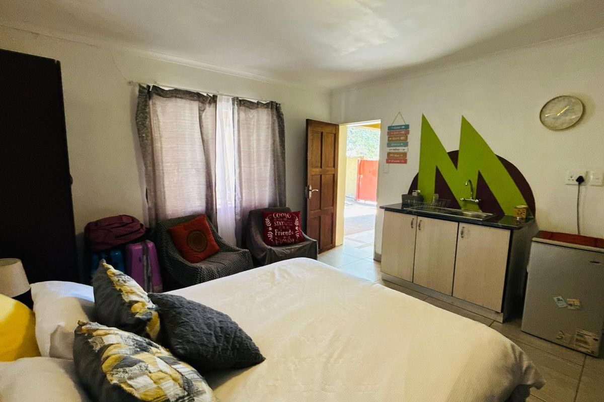 A bedroom featuring a small built-in kitchenette area with a sink and cabinet, tiled flooring, and direct access to an outdoor space.
