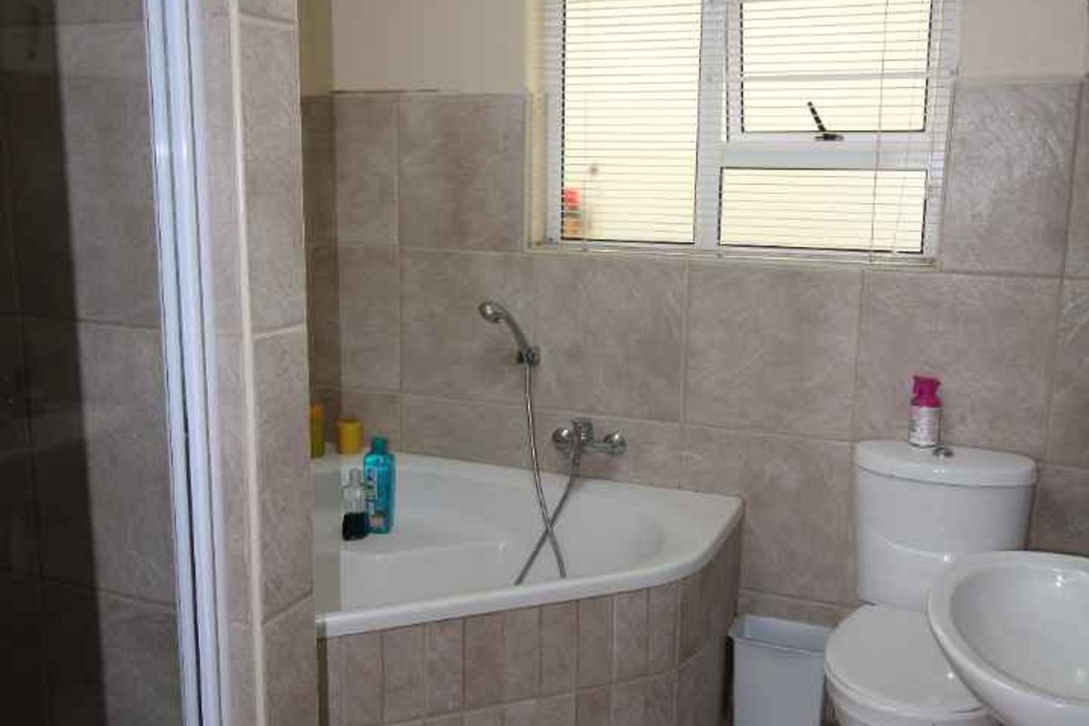 A functional bathroom featuring a corner bathtub, a separate shower enclosure, a pedestal basin, and a toilet with neutral wall and floor tiling.