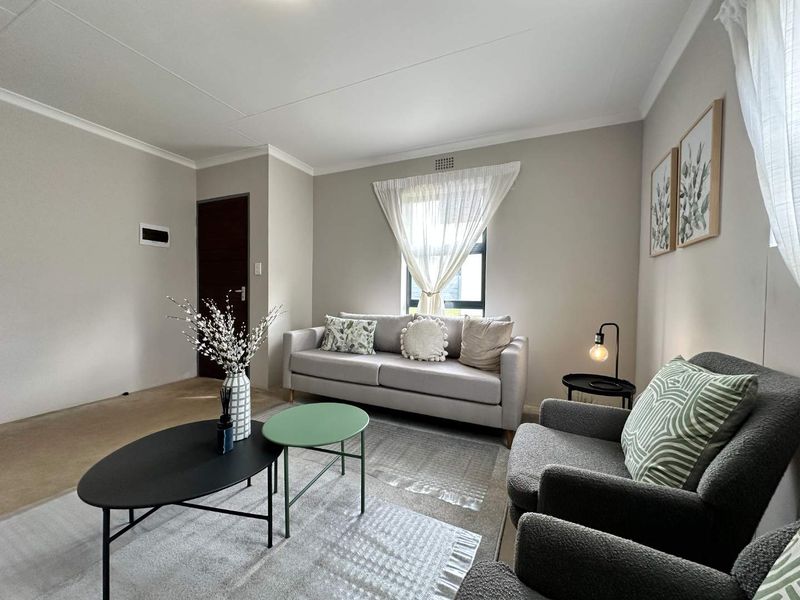 A well-maintained living room featuring neutral wall tones, cove cornicing, and a window providing natural light.