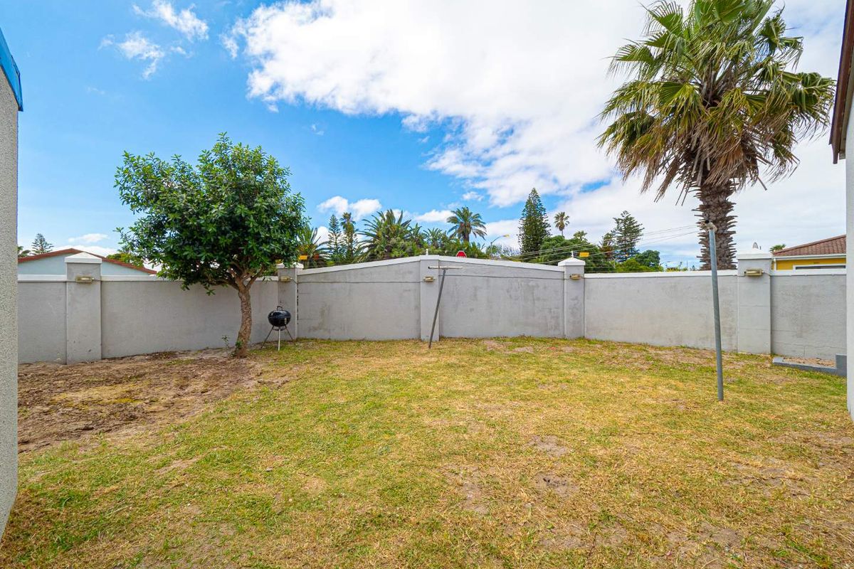 A private rear garden featuring a perimeter boundary wall, established palm tree, and open lawn space.