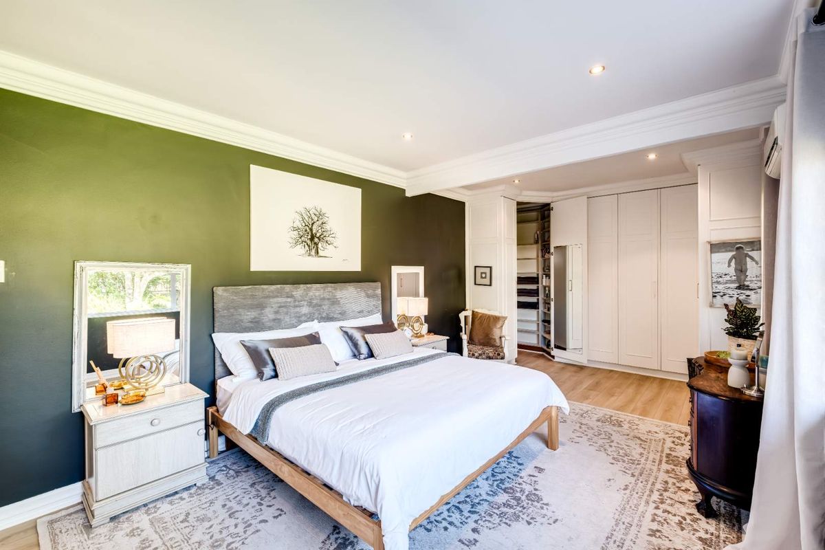 Spacious bedroom featuring built-in floor-to-ceiling wardrobes, recessed downlighting, crown molding, and a walk-in closet area with wood-style flooring.