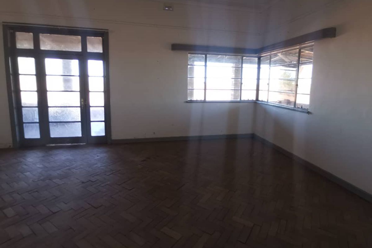 Spacious living area featuring original parquet flooring, large windows, and a glass-paneled door providing natural light and access to the exterior.
