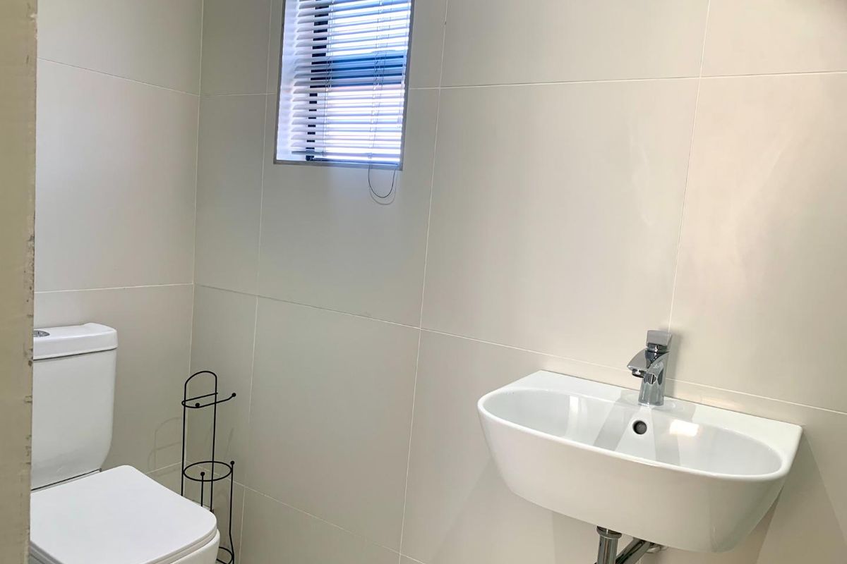 A clean and modern guest bathroom featuring a wall-mounted basin, chrome fixtures, and neutral wall tiling.