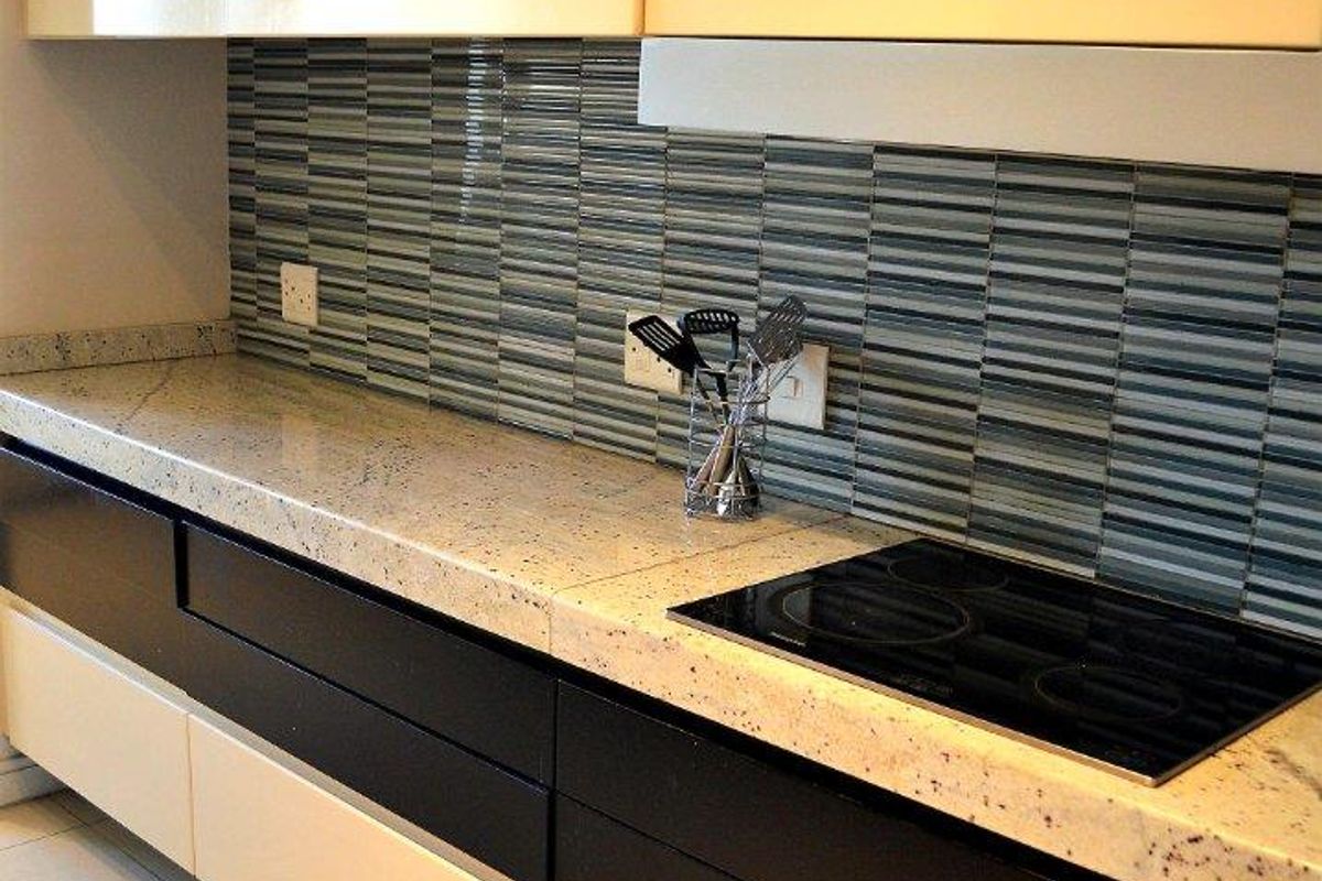 Modern kitchen featuring high-gloss cabinetry, speckled stone countertops, a built-in electric hob, and a decorative striped tile backsplash.