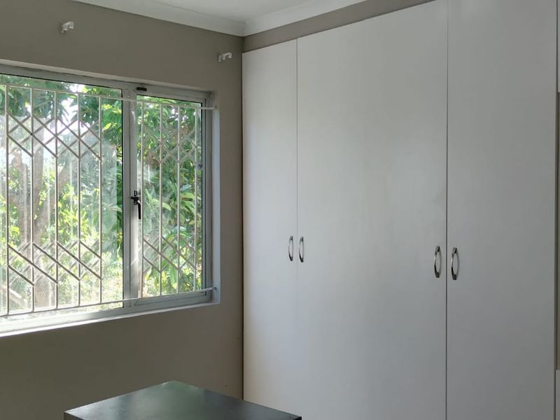 A bright bedroom featuring extensive built-in white cabinetry, a built-in vanity, and windows fitted with security bars.