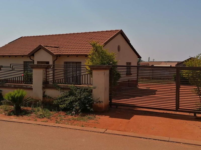 Front view of a single-story house featuring a tiled roof, perimeter wall with metal gate, and concrete pillars.