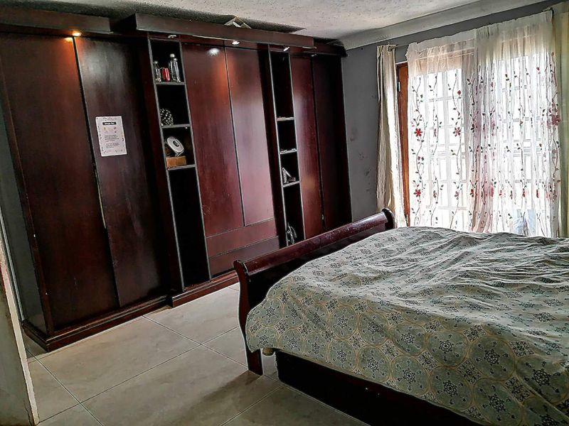A bedroom featuring dark wood built-in cupboards, tiled flooring, and access to the outdoors through glass-paned french doors.