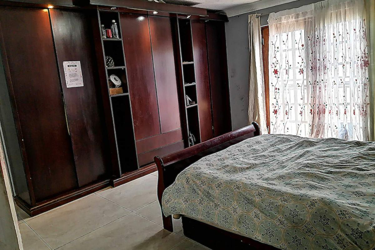 A bedroom featuring dark wood built-in cupboards, tiled flooring, and access to the outdoors through glass-paned french doors.