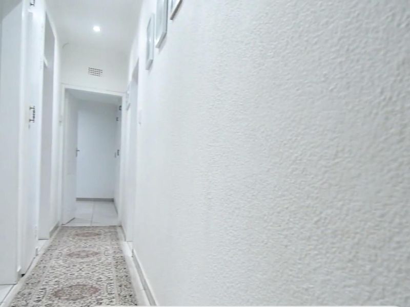 A bright, neutral hallway featuring tiled flooring and recessed lighting, providing access to multiple rooms within the home.