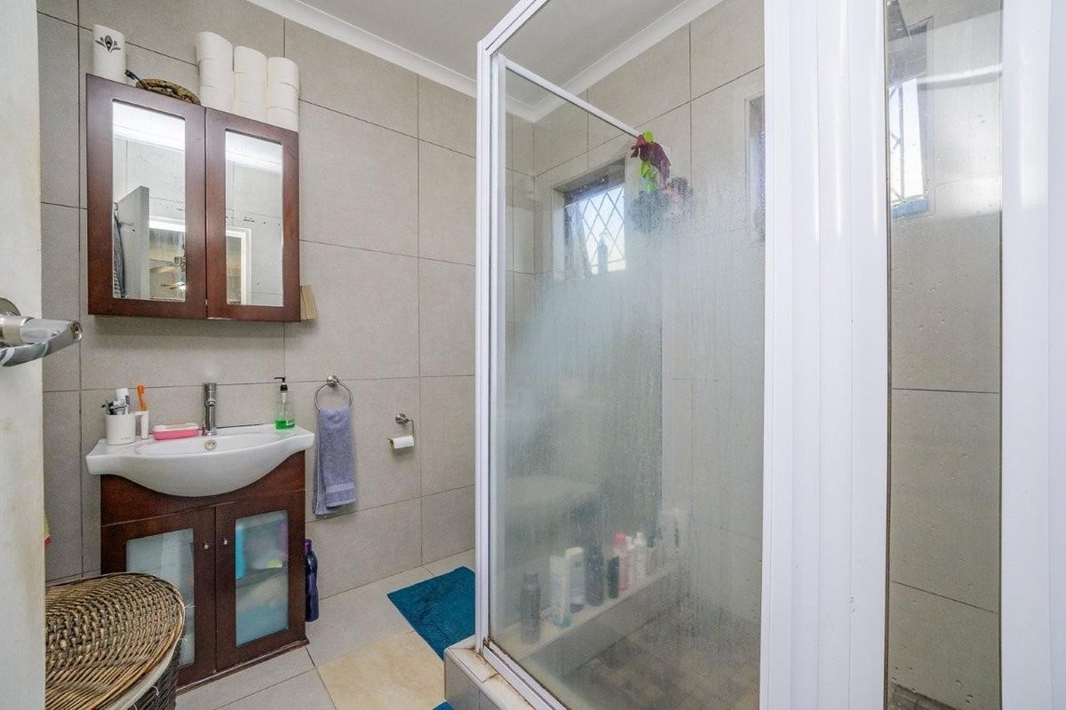 A functional bathroom featuring a vanity cabinet with basin, wall-mounted storage, and a glass-enclosed shower with tiled finishes.