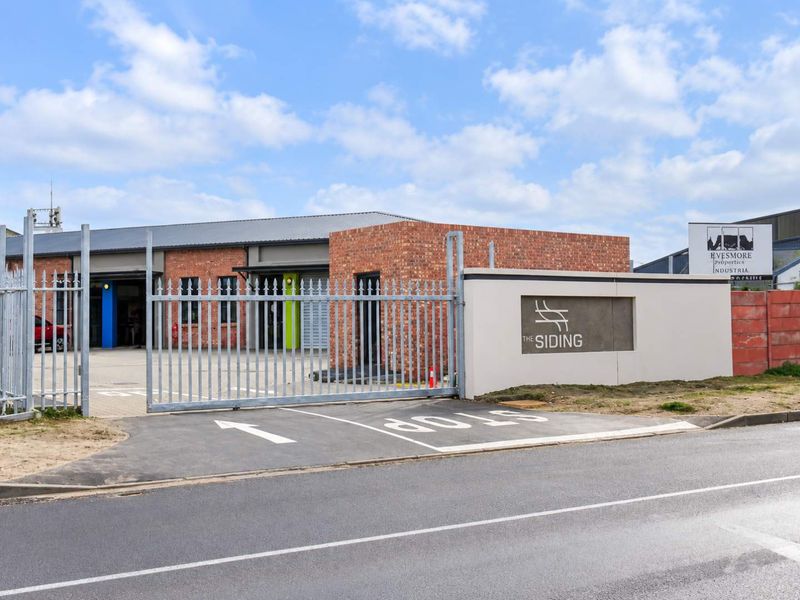 Front exterior view of The Siding industrial property featuring a secure gated entrance, brick facade, and paved driveway.