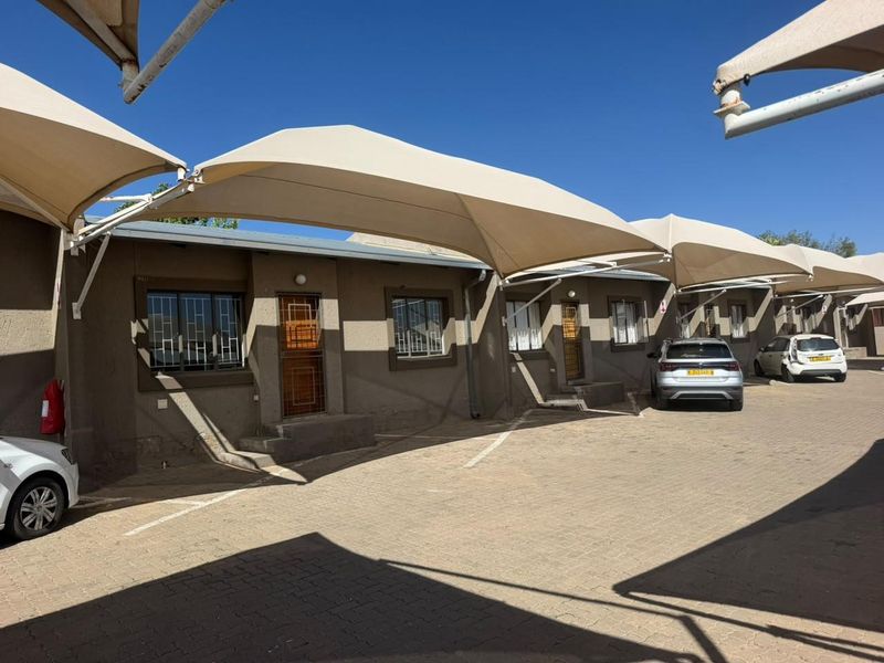 Front exterior view of the townhouse complex featuring paved parking areas with installed shade cloth carports and secure unit entrances.