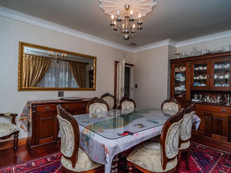 A formal dining room featuring classic crown molding, a decorative ceiling rose with a chandelier, and rich hardwood flooring.