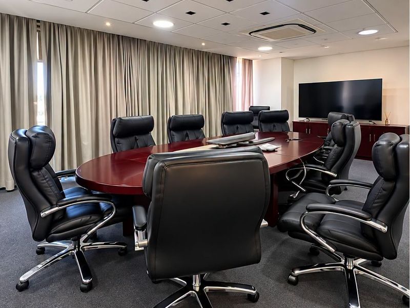 A professional boardroom featuring a large conference table, suspended ceiling with integrated lighting, ducted air conditioning, and built-in storage cabinetry.