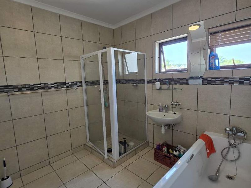 A functional bathroom featuring a shower enclosure, bathtub, wall-mounted basin, and neutral tiled finishes throughout.