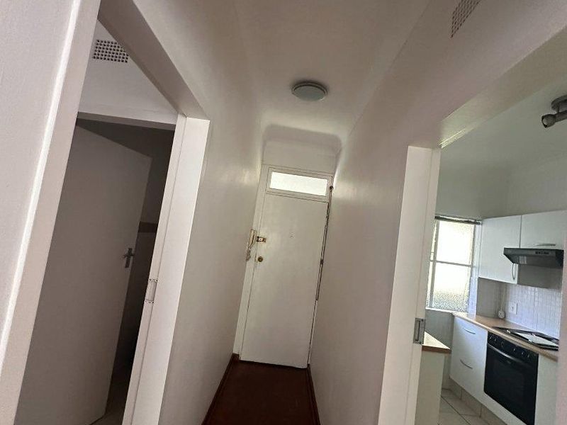 A functional apartment hallway connecting to a kitchen area, featuring a mix of parquet and tiled flooring with neutral wall finishes.