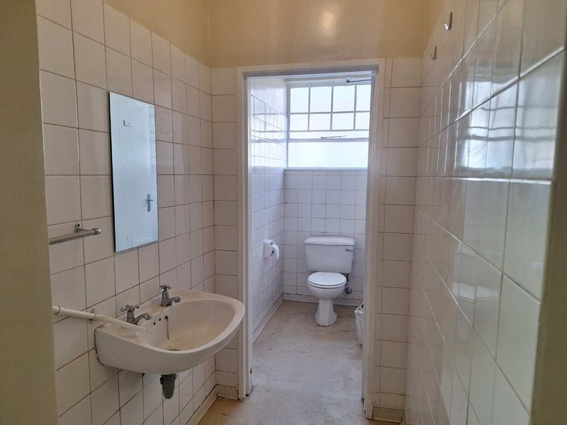 A functional office bathroom featuring a wall-mounted basin and a separate toilet cubicle with tiled walls throughout.