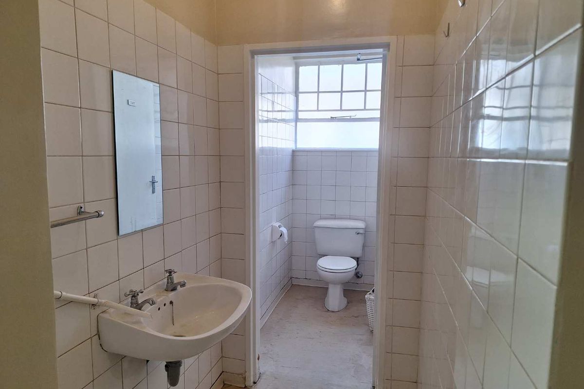 A functional office bathroom featuring a wall-mounted basin and a separate toilet cubicle with tiled walls throughout.