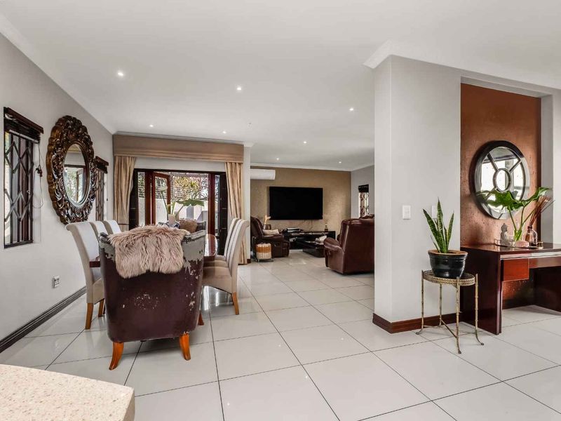Spacious open-plan living and dining area featuring neutral tiled flooring, recessed lighting, and a modern feature wall, creating a bright and cohesive living space.