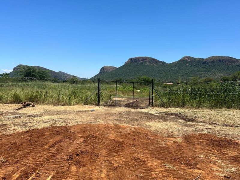 An undeveloped plot of land featuring a metal gate, natural vegetation, and scenic mountain views in the background.