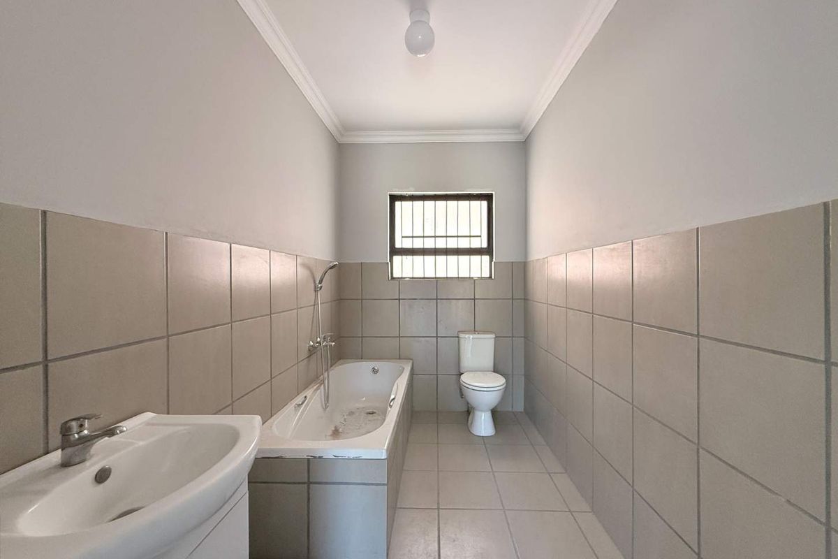 A functional bathroom featuring a built-in bathtub, pedestal basin, and toilet with neutral wall and floor tiling.