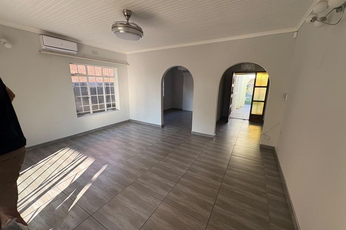 A bright, empty living room featuring wood-look tile flooring, a tongue and groove ceiling, and arched doorways leading to adjacent spaces.