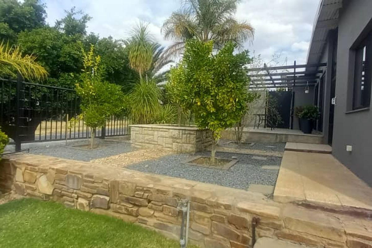 Rear garden area featuring a stone retaining wall, paved patio, pergola, and established landscaping with security fencing.