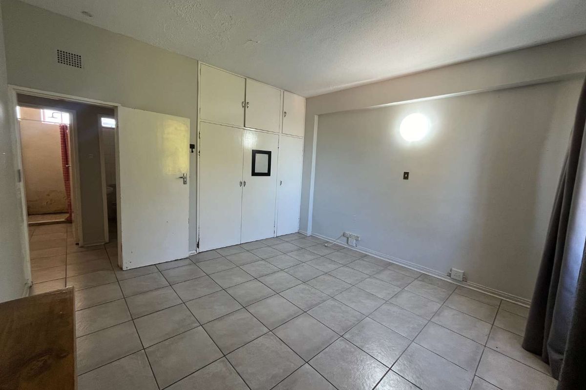A spacious bedroom featuring neutral floor tiles, built-in storage cupboards, and direct access to an adjacent bathroom.