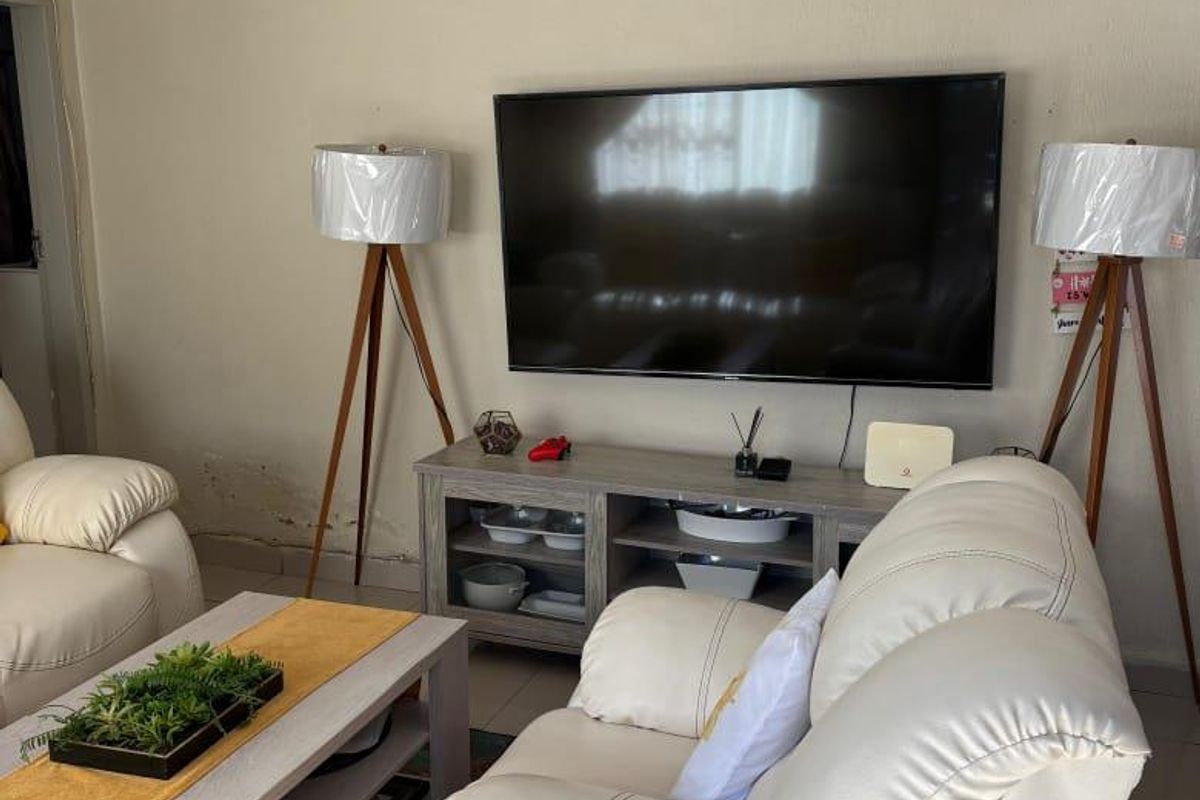 A living room featuring tiled flooring and a wall-mounted television, showing signs of moisture damage on the lower wall area.