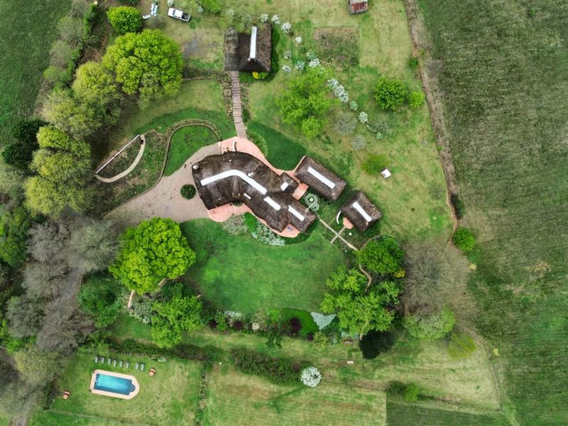 Aerial view of a property featuring a thatched roof main residence, outbuildings, a swimming pool, and extensive landscaped grounds.
