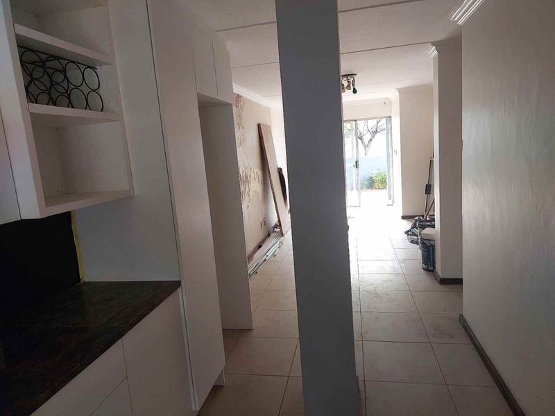 An open-plan living area featuring tiled floors and built-in cabinetry, currently undergoing renovation with visible wall damage requiring repair and finishing.
