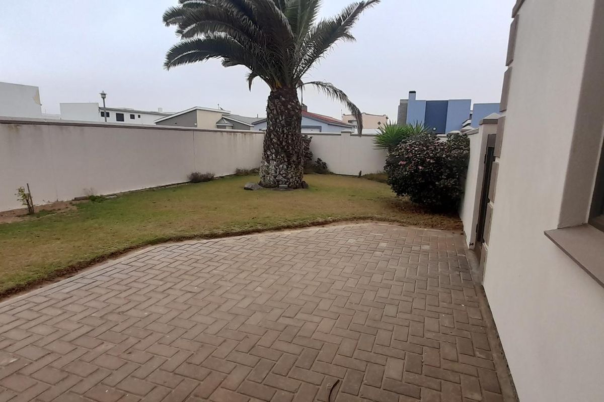 A rear exterior view featuring a paved patio area adjacent to a private garden with a boundary wall and established palm tree.