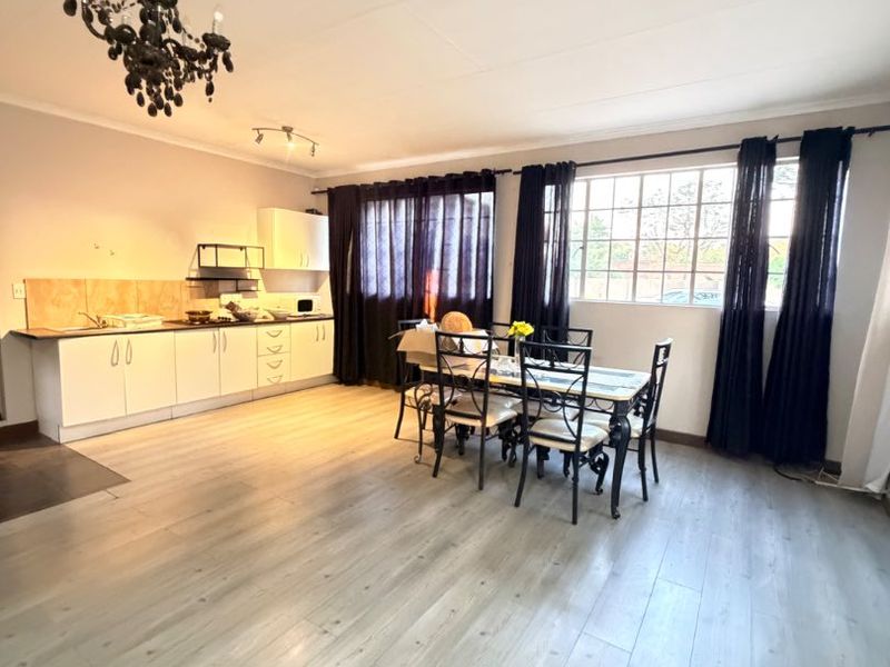 Open-plan living and kitchen area featuring light-toned laminate flooring, built-in cabinetry, and a large window providing natural light.
