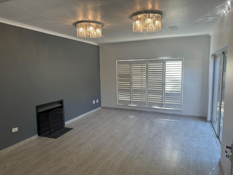 Spacious living room featuring light laminate flooring, a built-in fireplace, plantation shutters, and elegant crystal light fixtures, offering a bright and modern atmosphere.