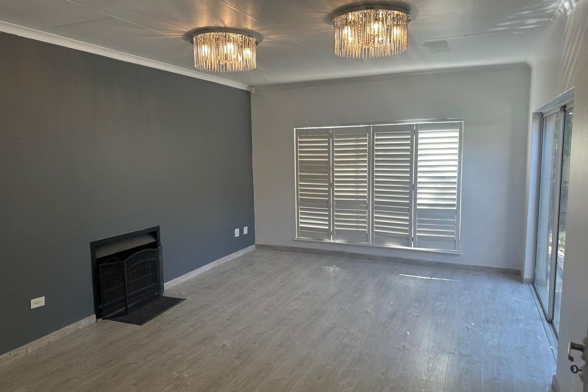 Spacious living room featuring light laminate flooring, a built-in fireplace, plantation shutters, and elegant crystal light fixtures, offering a bright and modern atmosphere.