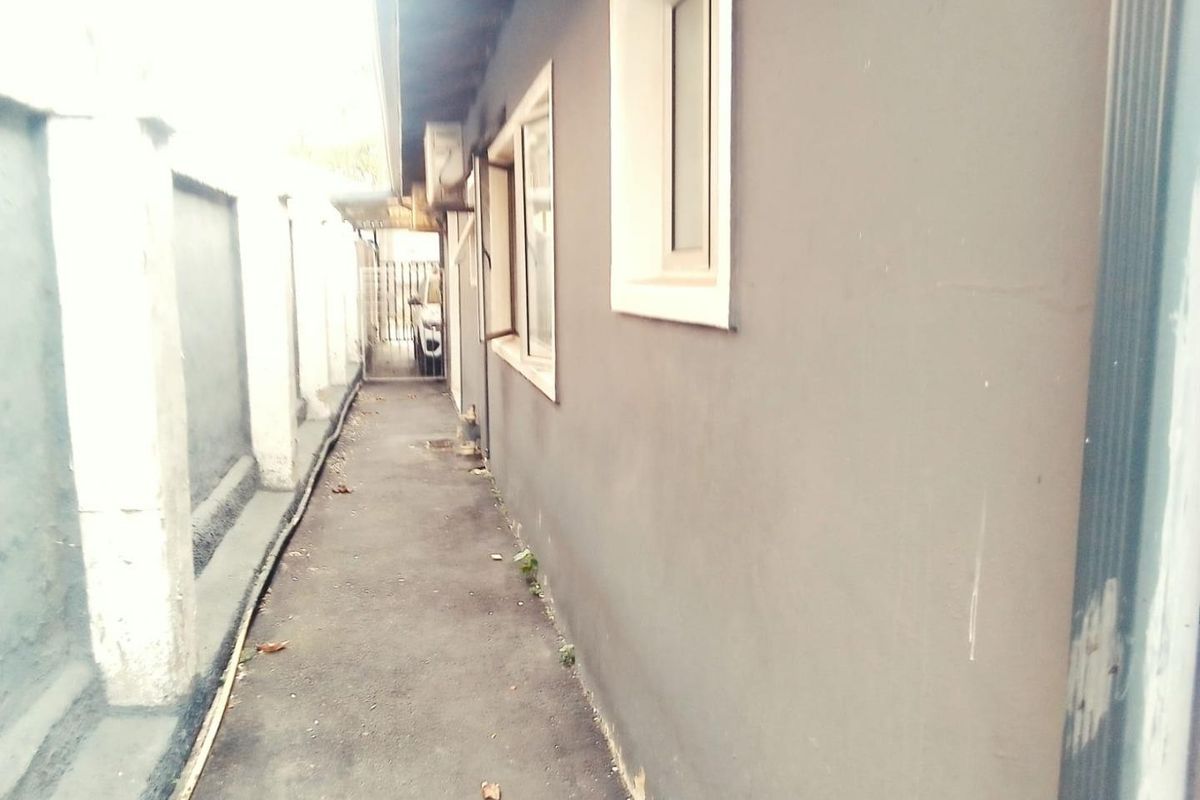 A narrow side passage or rear exterior walkway featuring a concrete path, boundary wall, and external window access.