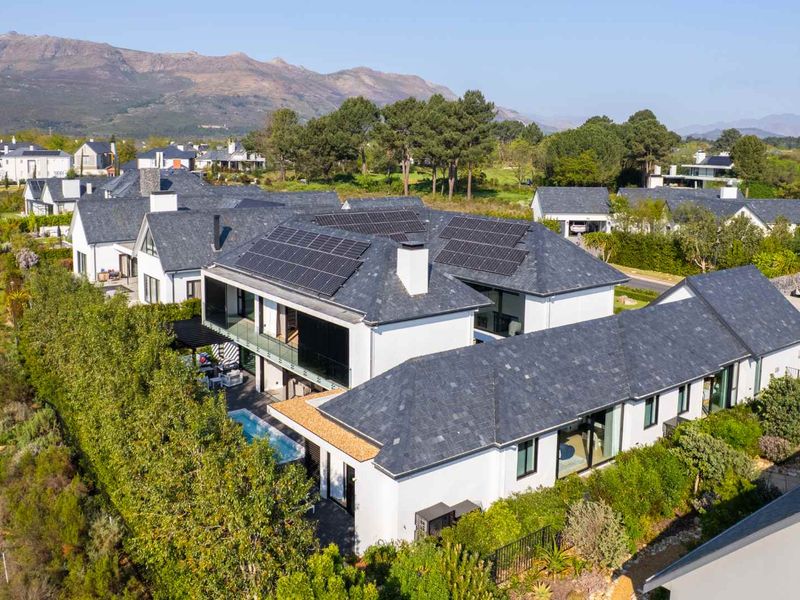 Aerial view of a modern residential property featuring a slate roof with integrated solar panels, a swimming pool, and landscaped surroundings.