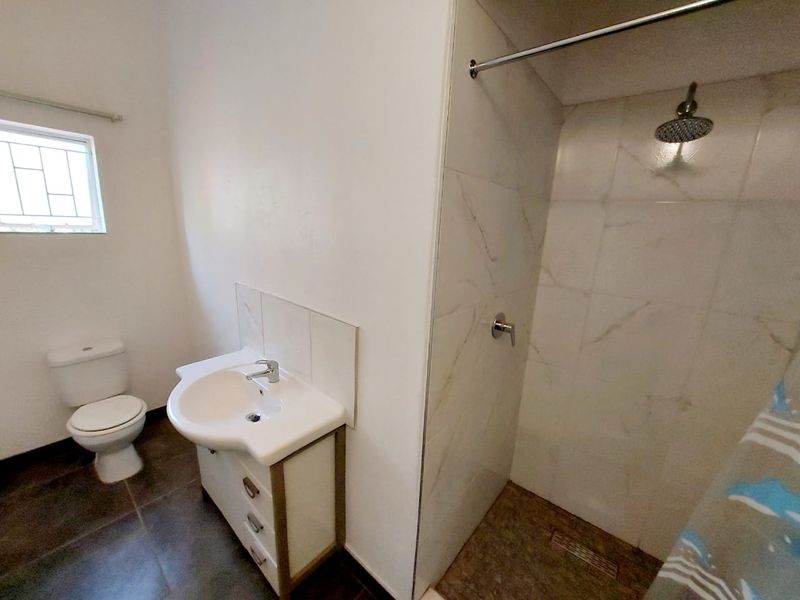 A clean, functional bathroom featuring a modern vanity, toilet, and a tiled shower enclosure with a rainfall shower head.