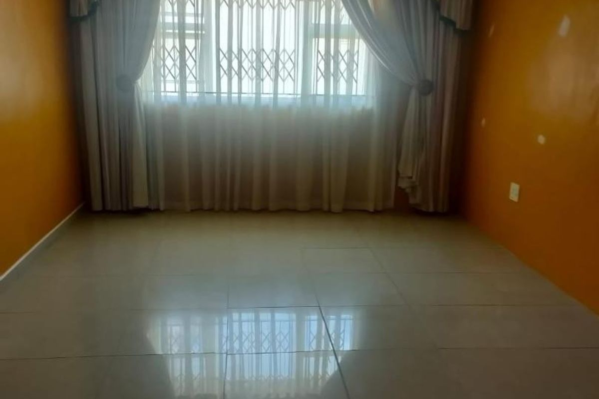 An empty living room featuring tiled flooring, a security gate on the window, and walls requiring cosmetic attention and repainting.