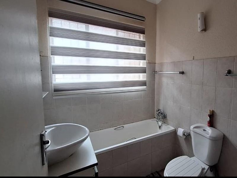 A functional bathroom featuring a bathtub, basin, and toilet with tiled walls and a roller blind.
